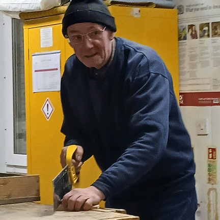 Man in beanie hat sawing wood.
